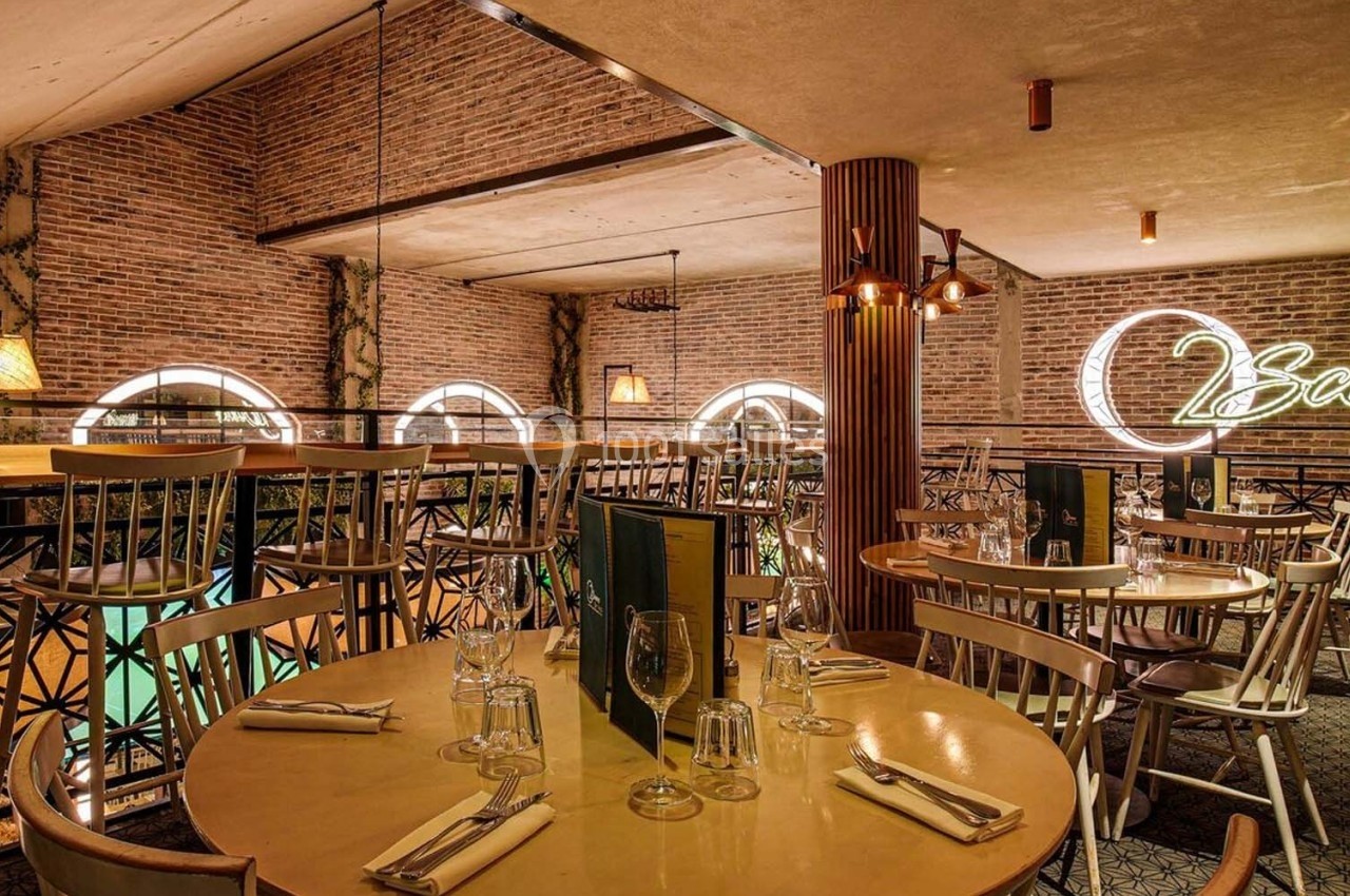 Salle de restaurant avec murs en briques, tables dressées et enseigne lumineuse ’Scenes’ sur le mur.