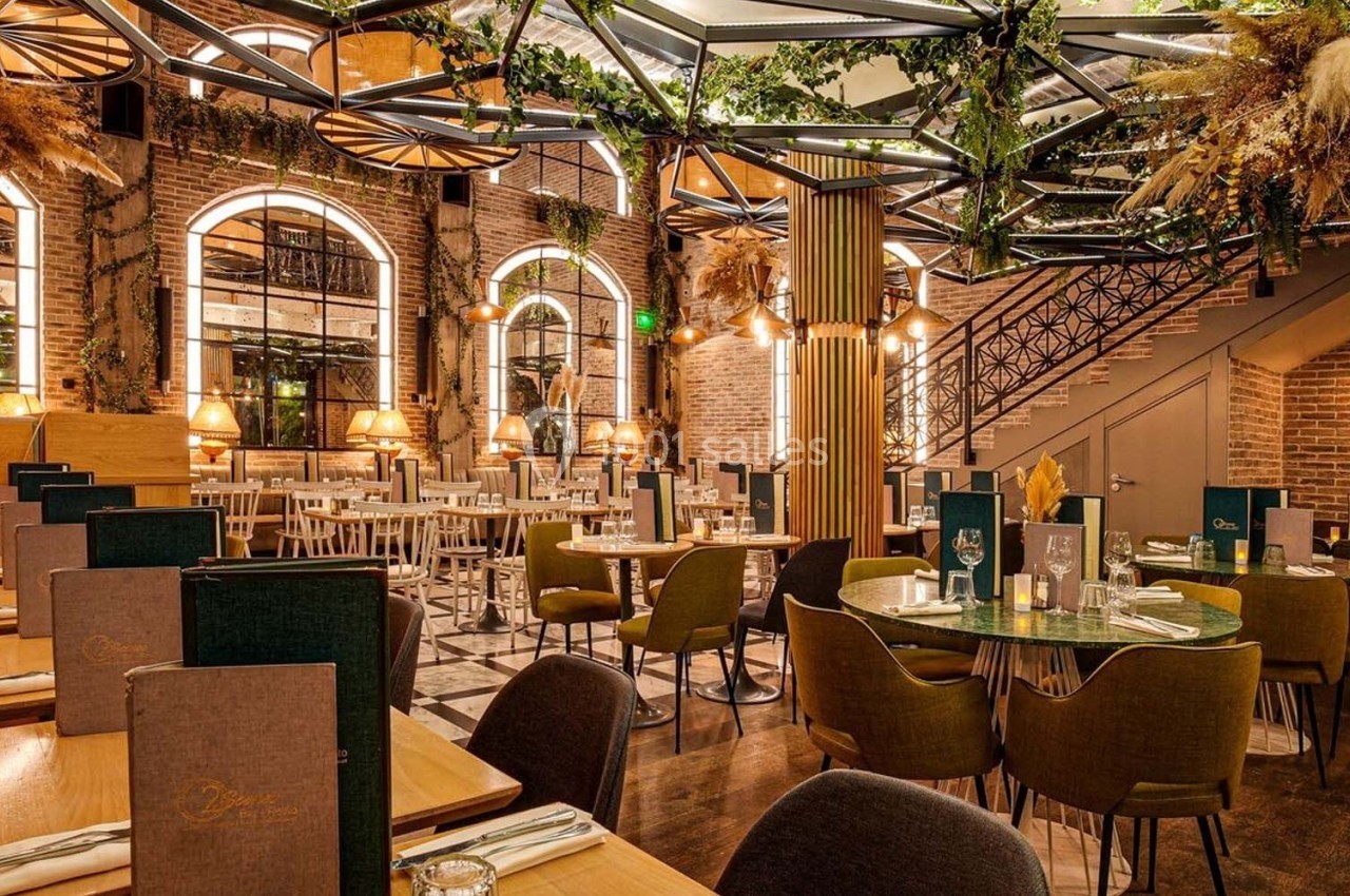 Salle de restaurant élégante avec tables dressées, décoration végétale et éclairage chaleureux.