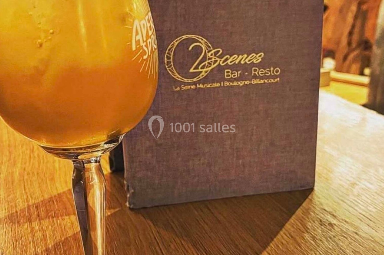 Verre de cocktail orange posé sur une table en bois, avec un menu violet d'un bar-restaurant en arrière-plan.