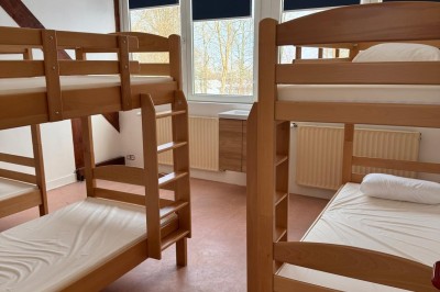 Chambre avec deux lits superposés en bois, fenêtres avec stores bleus et murs blancs.