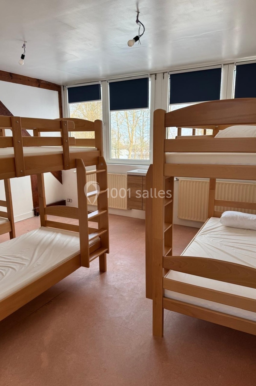 Chambre avec deux lits superposés en bois, fenêtres avec stores bleus et murs blancs.