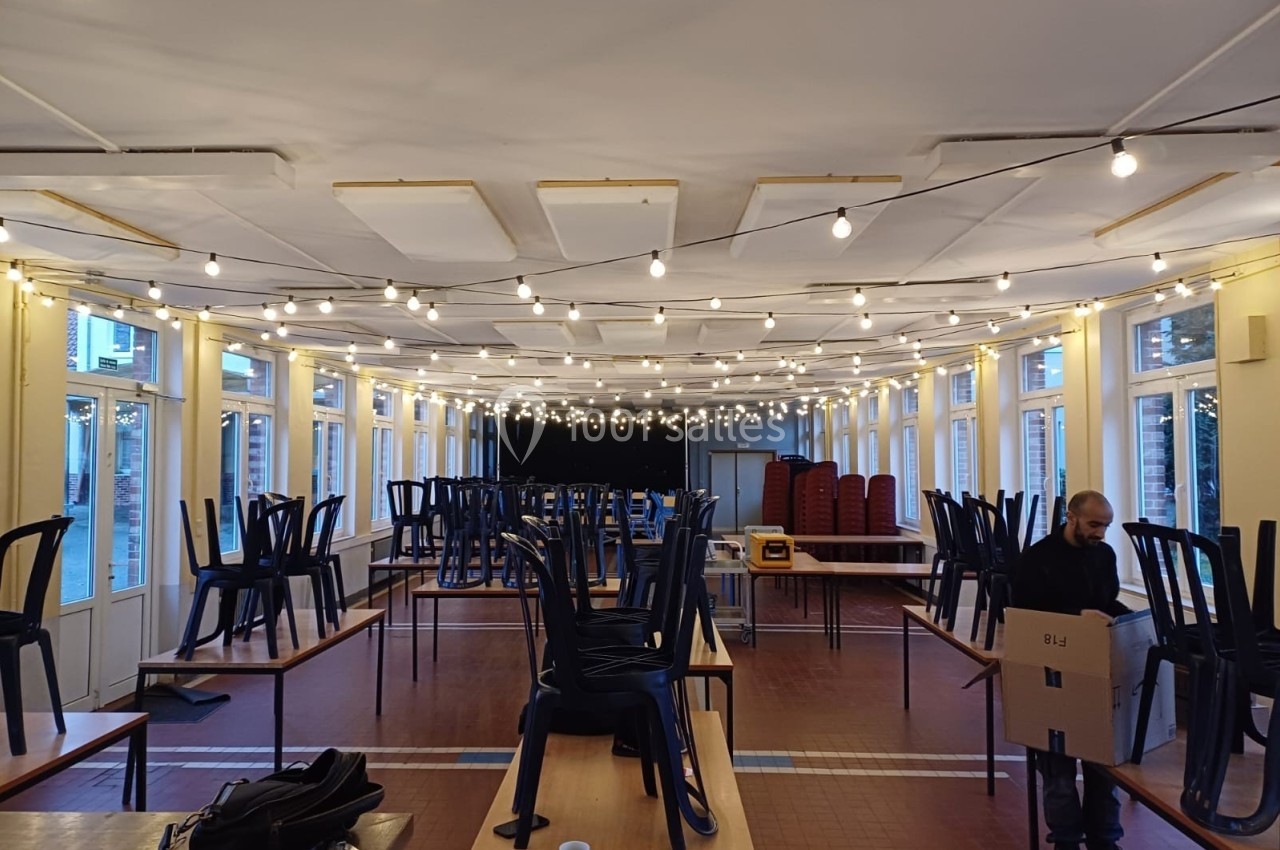 Salle lumineuse en préparation, avec des chaises empilées sur des tables et une personne portant un carton.
