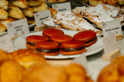 Façade d'un salon de thé parisien avec une devanture noire, une enseigne beige et des chaises en terrasse.