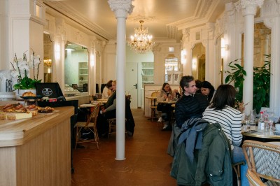 Façade d'un salon de thé parisien avec une devanture noire, une enseigne beige et des chaises en terrasse.