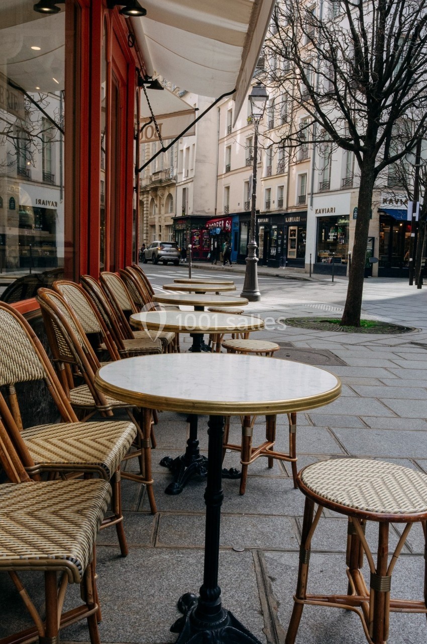 Terrasse de café parisien avec tables rondes en marbre et chaises en rotin, bordant une rue calme.