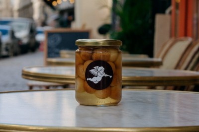 Façade d'un salon de thé parisien avec une devanture noire, une enseigne beige et des chaises en terrasse.