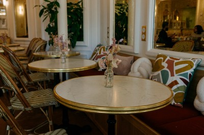 Façade d'un salon de thé parisien avec une devanture noire, une enseigne beige et des chaises en terrasse.