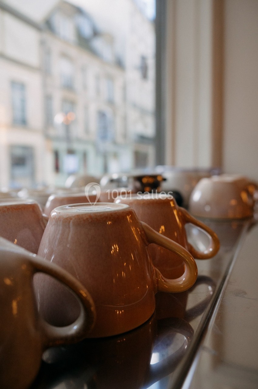 Tasses en céramique retournées sur un plateau en métal près d'une fenêtre donnant sur des bâtiments urbains.