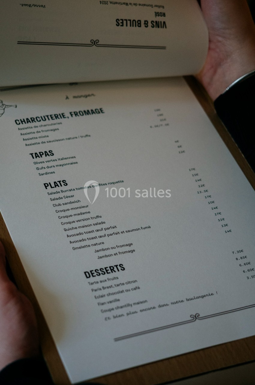 Menu imprimé tenu par une personne, listant des plats, tapas, desserts, et options de charcuterie et fromage.