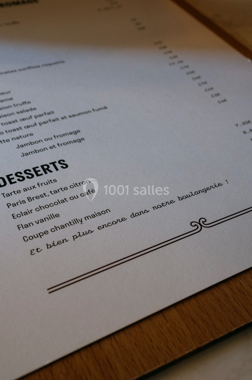 Carte de menu en papier posée sur une table, avec une section dédiée aux desserts et une note manuscrite en bas.
