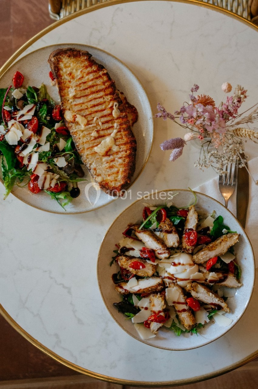 Assiette de salade avec poulet grillé et tomates cerises, accompagnée d'une tartine gratinée sur une table en marbre.