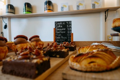 Façade d'un salon de thé parisien avec une devanture noire, une enseigne beige et des chaises en terrasse.