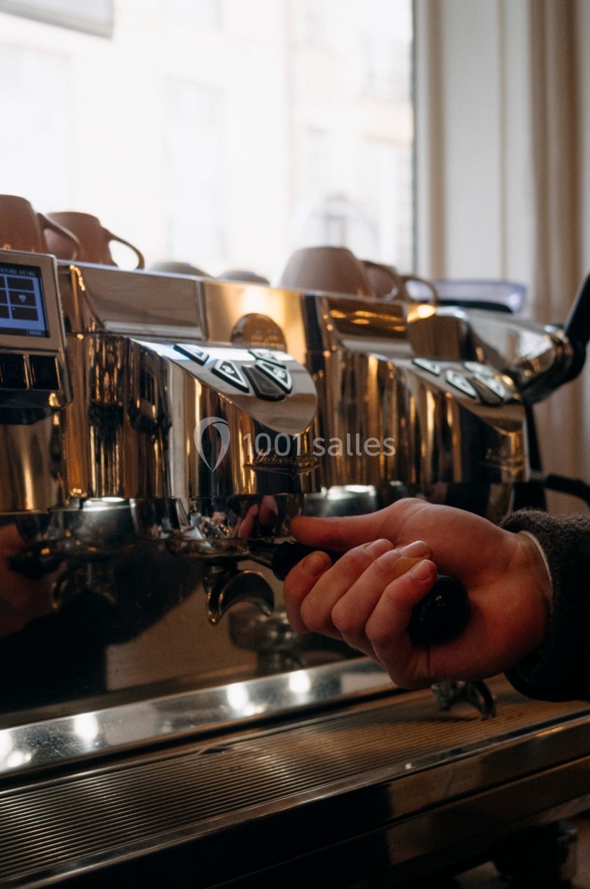 Une main prépare un café en manipulant le porte-filtre d'une machine à expresso professionnelle dans un café.