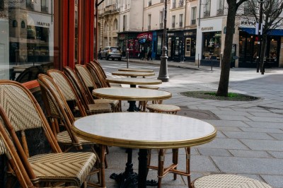Façade d'un salon de thé parisien avec une devanture noire, une enseigne beige et des chaises en terrasse.
