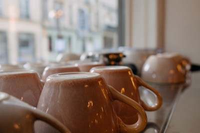 Façade d'un salon de thé parisien avec une devanture noire, une enseigne beige et des chaises en terrasse.