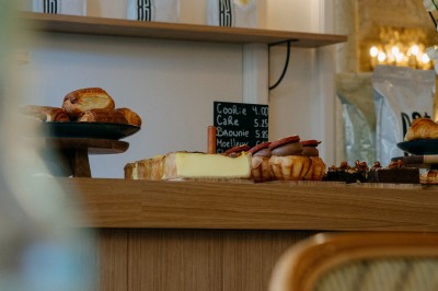 Façade d'un salon de thé parisien avec une devanture noire, une enseigne beige et des chaises en terrasse.