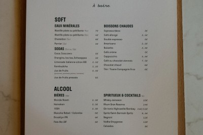 Façade d'un salon de thé parisien avec une devanture noire, une enseigne beige et des chaises en terrasse.