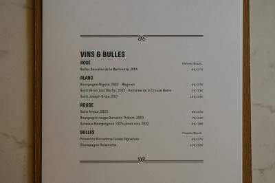 Façade d'un salon de thé parisien avec une devanture noire, une enseigne beige et des chaises en terrasse.