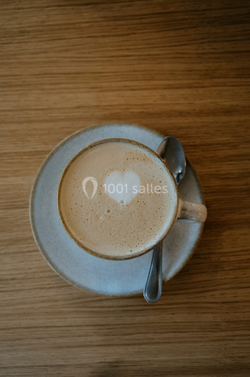 Tasse de café latte avec un motif en forme de cœur dans la mousse, posée sur une soucoupe avec une cuillère.