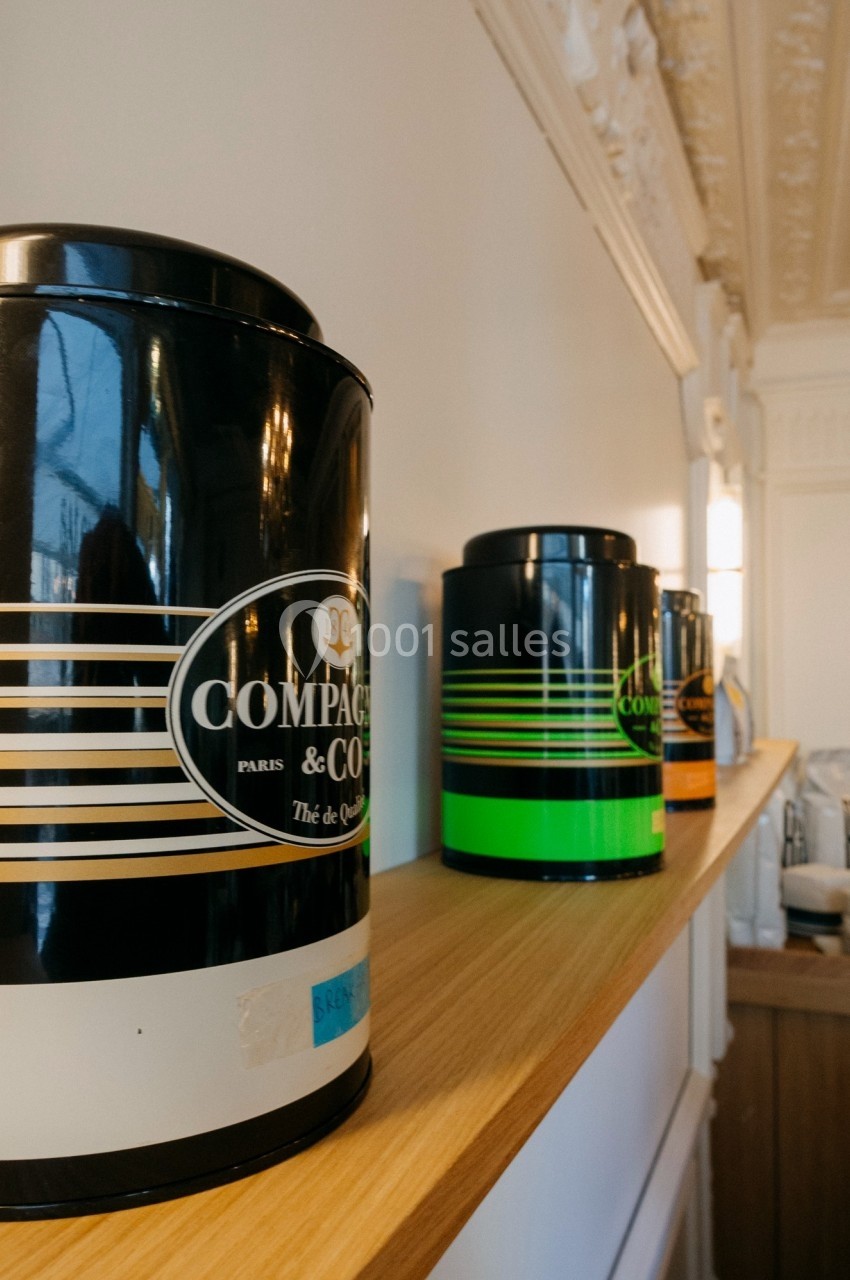 Boîtes de thé colorées alignées sur une étagère en bois dans un intérieur lumineux avec moulures au plafond.