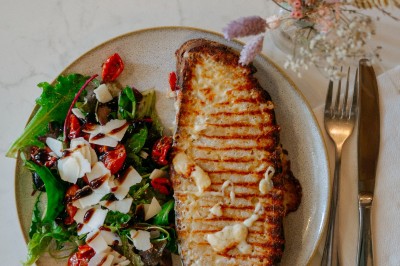 Façade d'un salon de thé parisien avec une devanture noire, une enseigne beige et des chaises en terrasse.