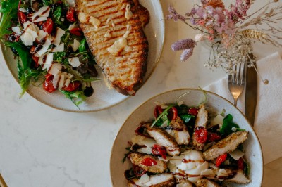 Façade d'un salon de thé parisien avec une devanture noire, une enseigne beige et des chaises en terrasse.