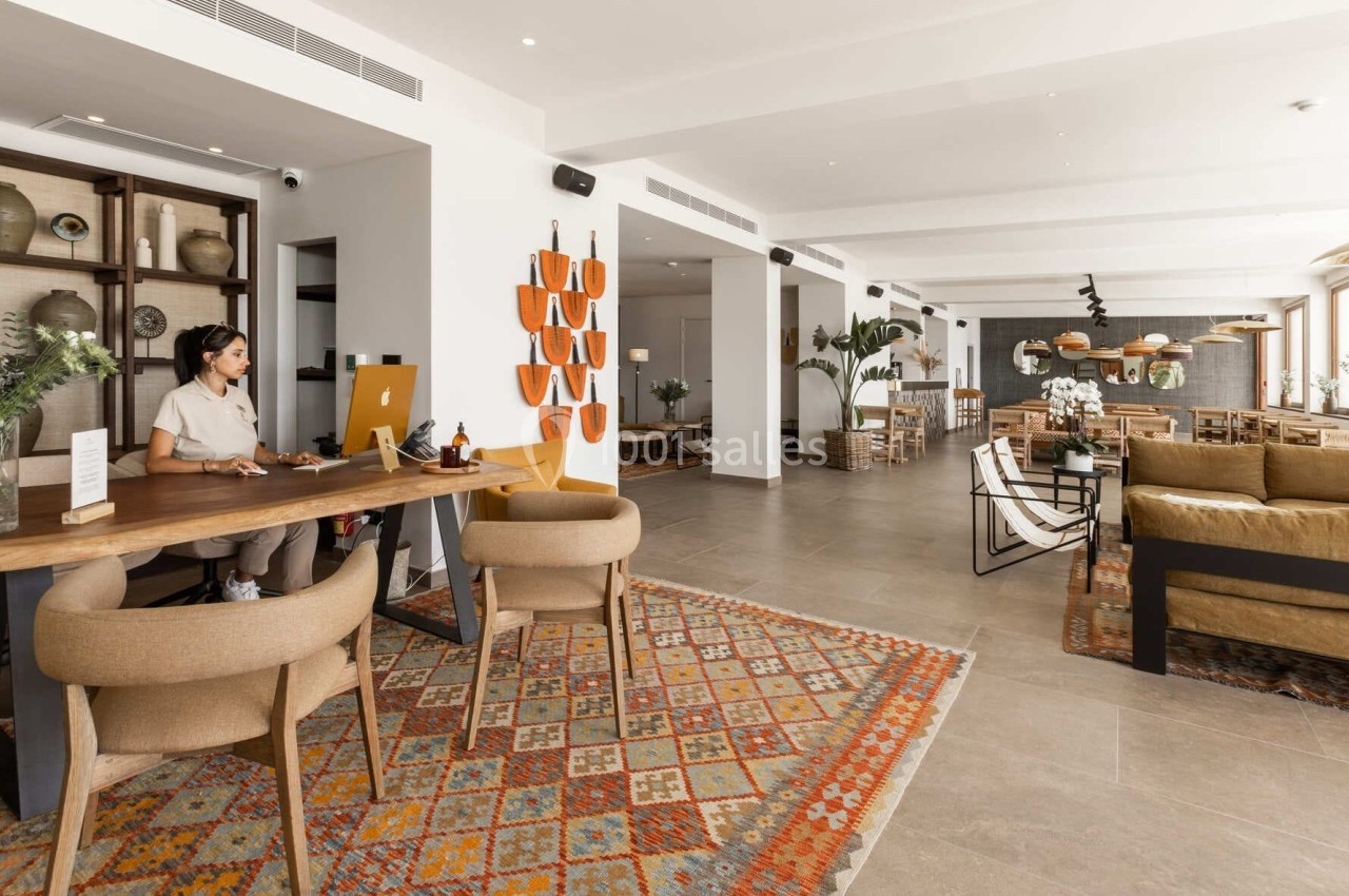 Espace intérieur lumineux avec un bureau d'accueil, des fauteuils, des tapis colorés et un coin salon moderne.