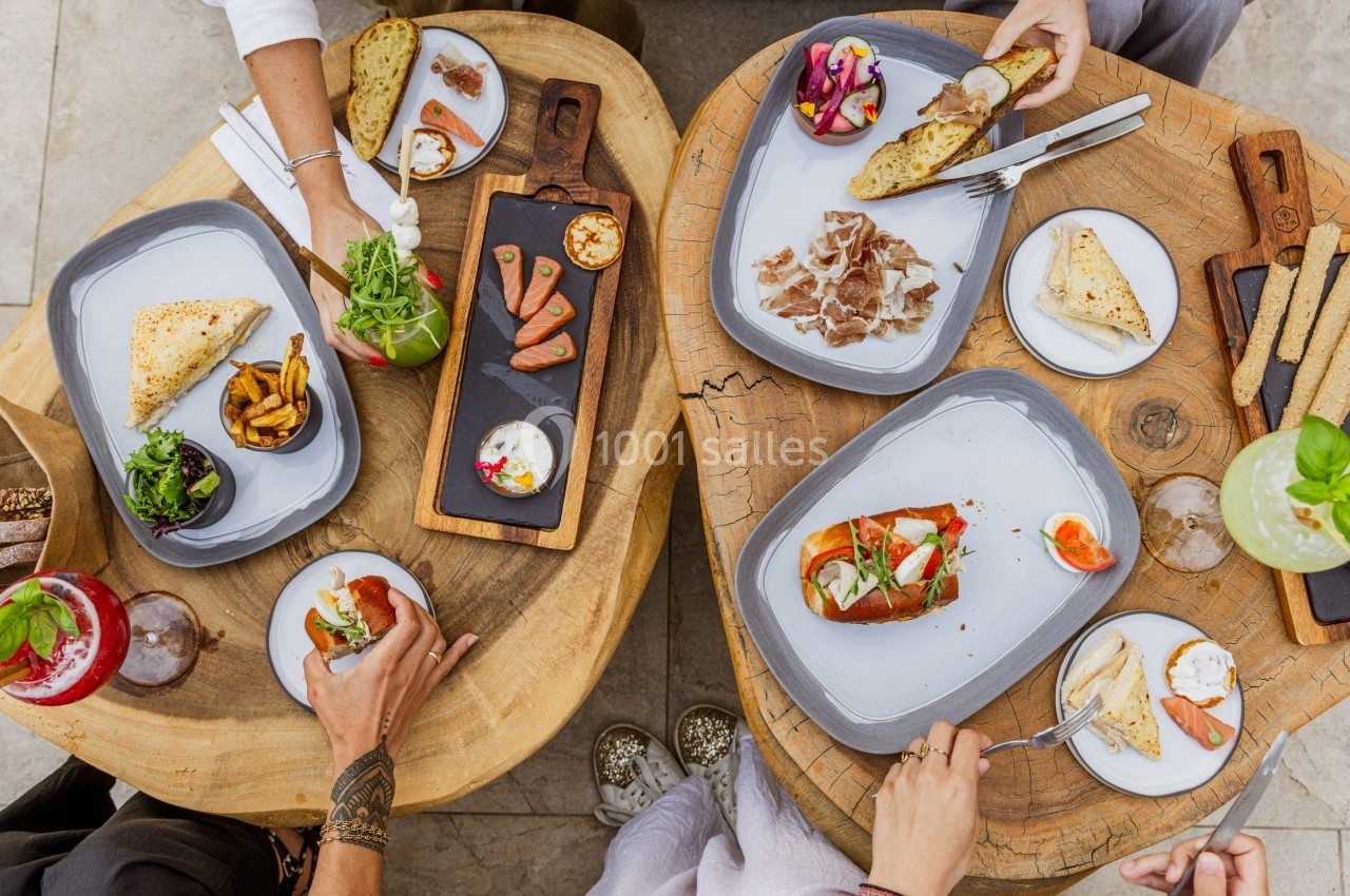 Vue de dessus de deux tables en bois avec des assiettes de tapas, boissons et mains en train de partager un repas.