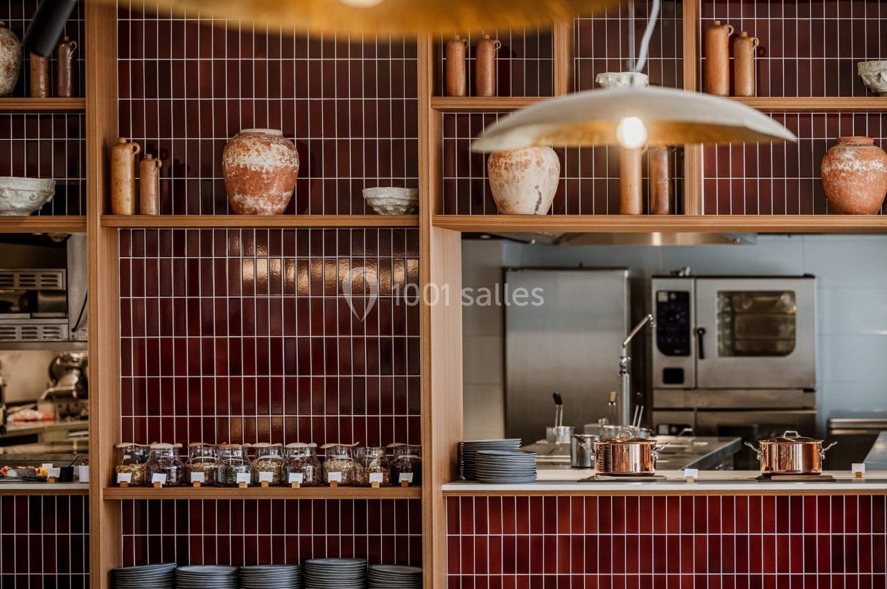 Étagères en bois avec pots en terre cuite et vaisselle, devant une cuisine ouverte avec four professionnel.