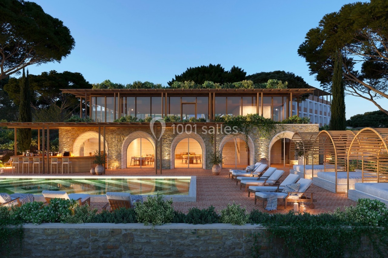 Villa moderne avec façade en pierre, grandes baies vitrées, piscine éclairée et terrasse aménagée entourée de végétation.