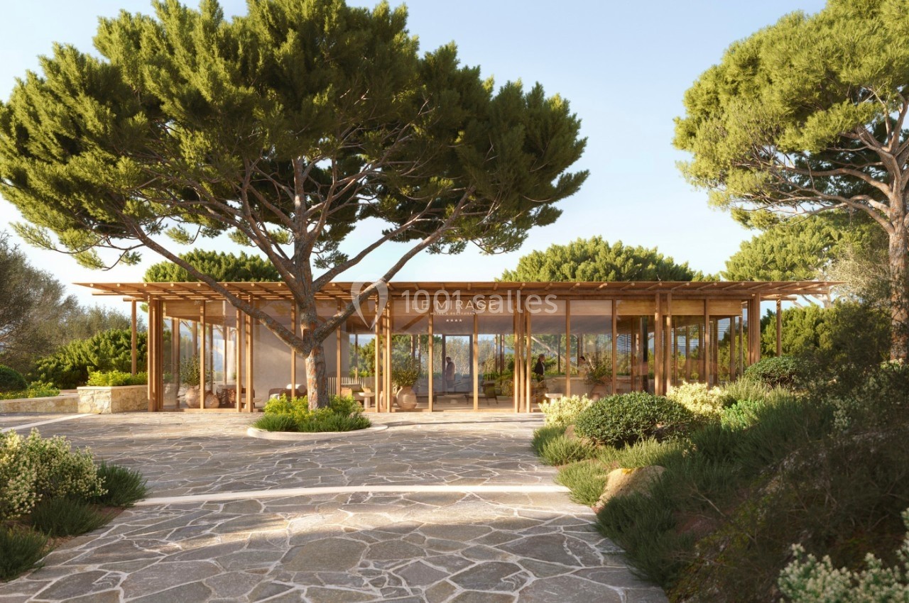 Pavillon en bois entouré de végétation méditerranéenne avec des pins et un sol en pierre sous un ciel dégagé.