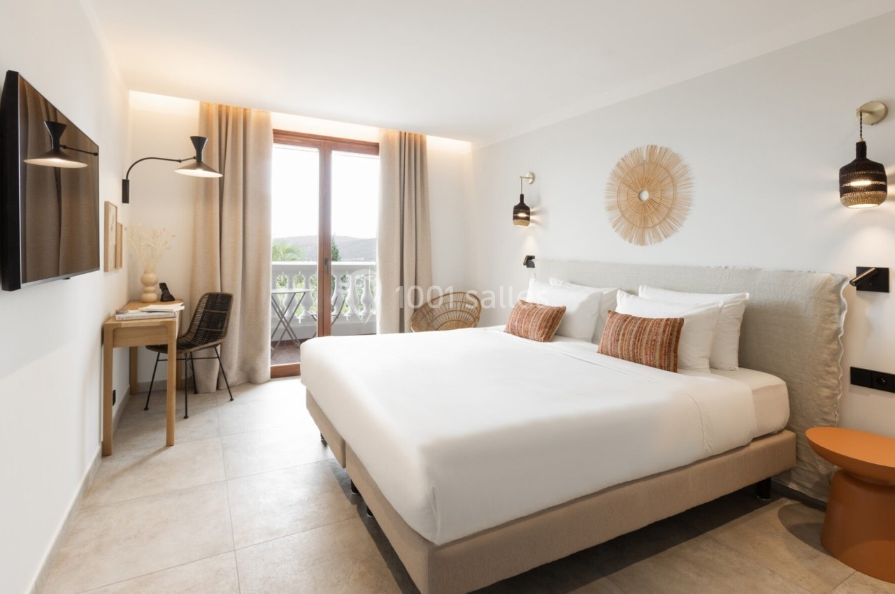 Chambre lumineuse avec lit double, bureau, balcon avec vue sur l'extérieur et décoration moderne aux tons neutres.