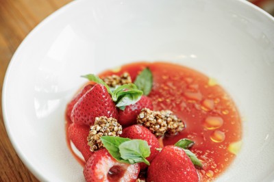 Femme buvant un cocktail rouge avec une paille, en extérieur, cheveux blonds au vent.