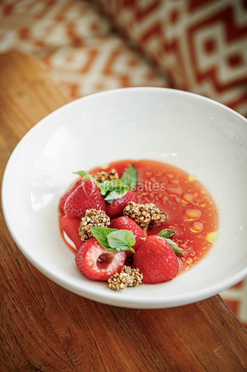 Bol de fraises fraîches avec graines croustillantes, feuilles de menthe et sauce rouge, posé sur une table en bois.