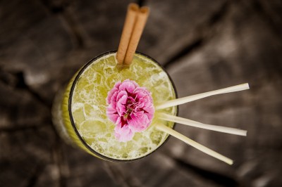 Femme buvant un cocktail rouge avec une paille, en extérieur, cheveux blonds au vent.