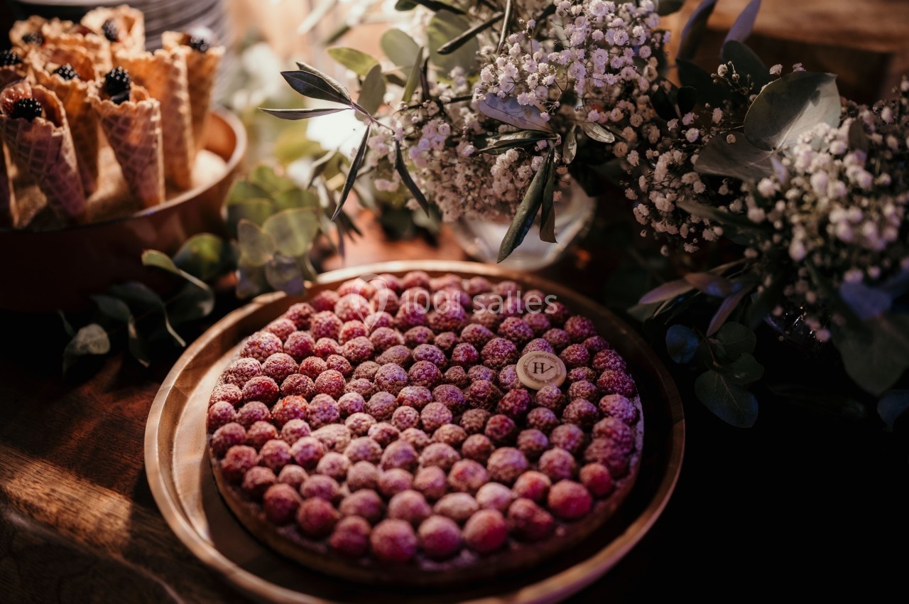 Tarte aux framboises sur une table en bois, entourée de fleurs blanches et de cornets garnis de fruits.