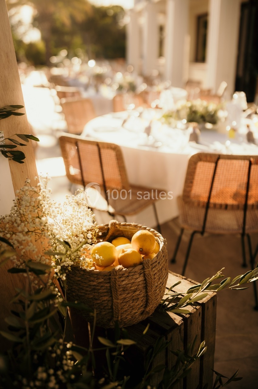 Panier de citrons posé sur une caisse en bois, avec des tables décorées en arrière-plan dans un cadre extérieur ensoleillé.