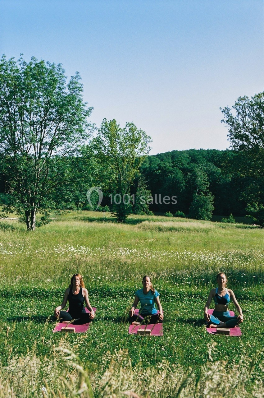 Trois personnes assises en tailleur sur des tapis de yoga dans un champ verdoyant par une journée ensoleillée.