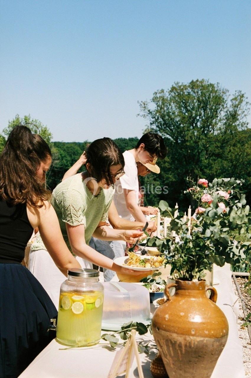 Des personnes se servent de nourriture sur une table extérieure décorée de fleurs et de boissons, par une journée…