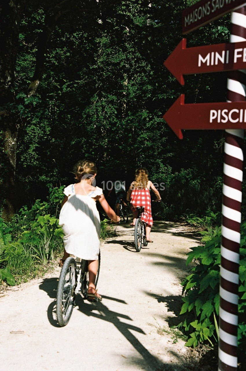 Deux enfants à vélo sur un chemin forestier, près de panneaux indiquant des directions touristiques.