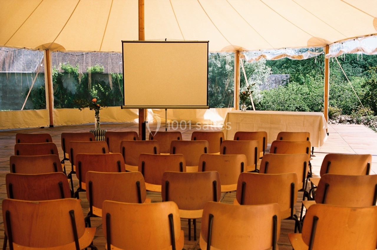 Chaises alignées face à un écran de projection dans une tente lumineuse avec vue sur un jardin.