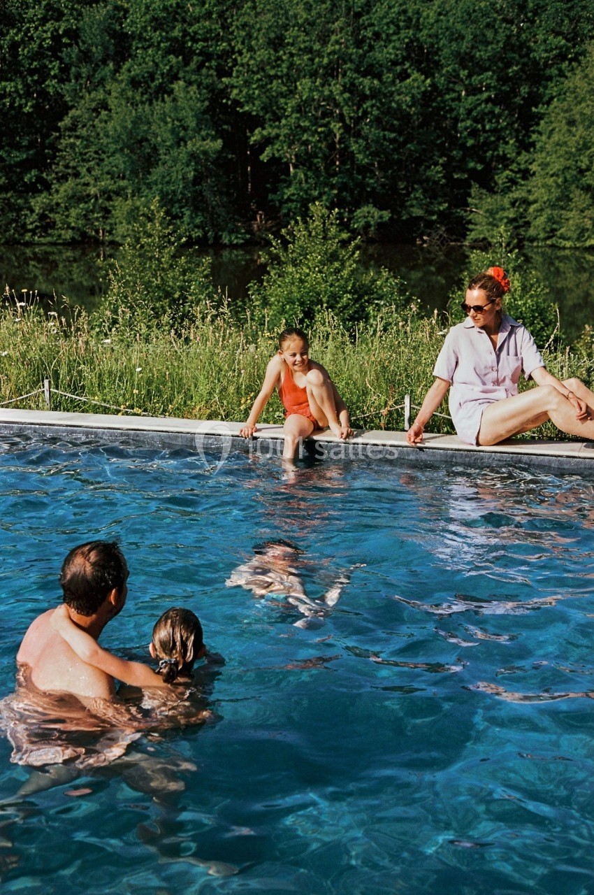 Une famille profite d'une piscine extérieure entourée de verdure par une journée ensoleillée.