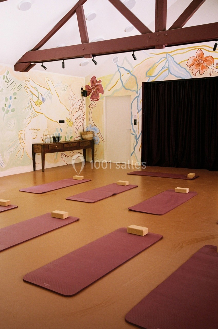 Salle de yoga avec tapis violets alignés, briques en bois et mur décoré de peintures florales et abstraites.