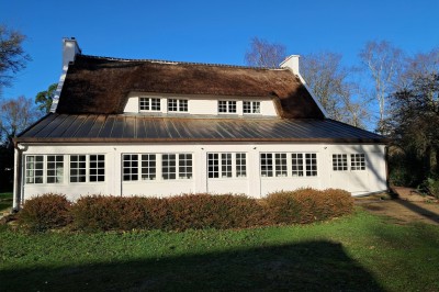 Abri en bois avec toit en pente, sol en gravier et clôture attenante, entouré de végétation et d'herbe.