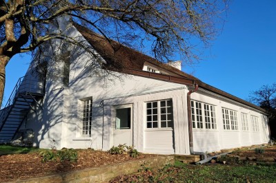 Abri en bois avec toit en pente, sol en gravier et clôture adjacente, situé dans un environnement arboré.