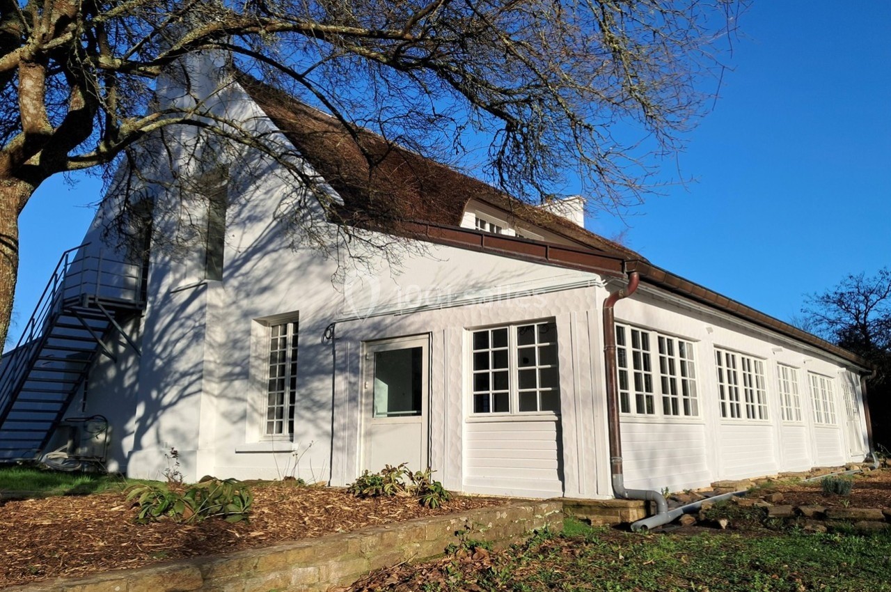 Façade d'une maison blanche avec des fenêtres à carreaux, un toit en pente et un escalier extérieur métallique.