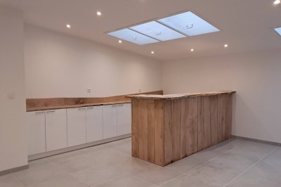 Abri en bois avec toit en pente, sol en gravier et clôture adjacente, situé dans un environnement arboré.