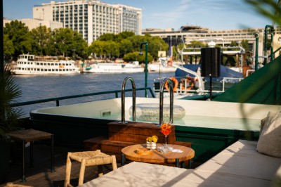 Miniature Location salle Paris 5 (Paris) - Péniche Amour #8 Terrasse aménagée sur une péniche avec vue sur la Seine, des bâtiments et un pont en arrière-plan.