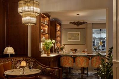 Chambre lumineuse avec lit double, fauteuil jaune, commode en bois et grande fenêtre donnant sur des immeubles parisiens.