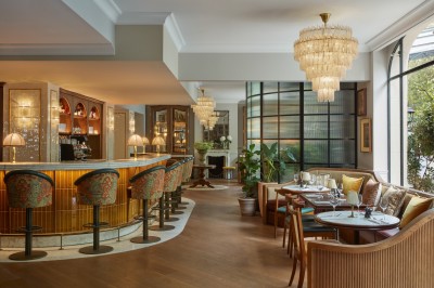 Chambre lumineuse avec lit double, fauteuil jaune, commode en bois et grande fenêtre donnant sur des immeubles parisiens.